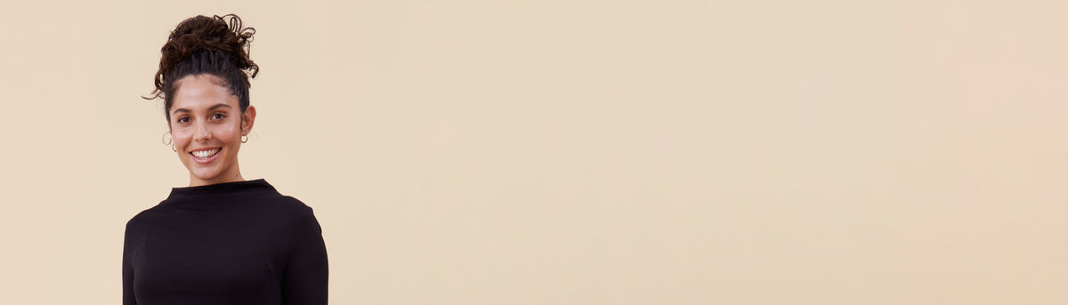 Työmekko hymyilevän tummahiuksisen työntekijän yllä, beige tausta